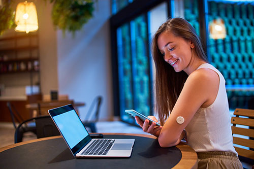 women sitting at desk with laptop, showing wearable monitor on arm