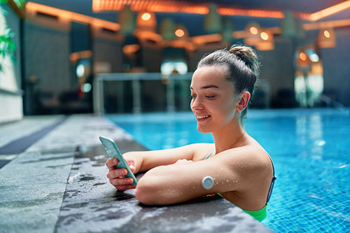 woman standing in swimming pool looking at phone, wearable monitor on arm