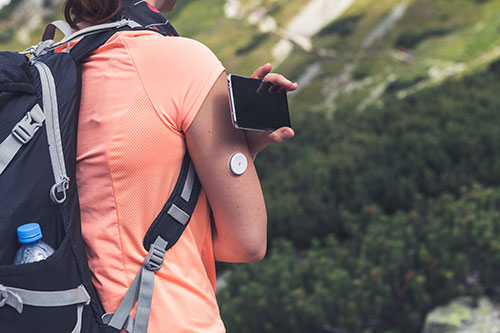 person hiking in mountains holding iphone near arm monitor